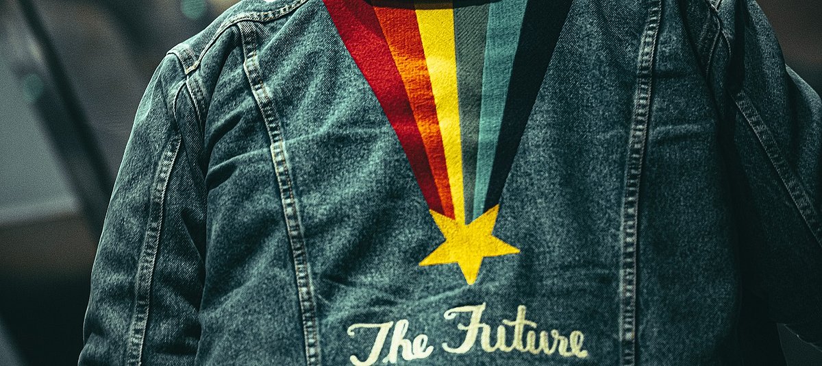 Eine Jeansjacke von hinten, mit einem Stern, der einen bunten Schweif hinter sich her zieht und der Aufschrift The Future