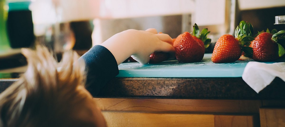Ein Kind greift nach Erdbeeren, die auf einem Tisch liegen