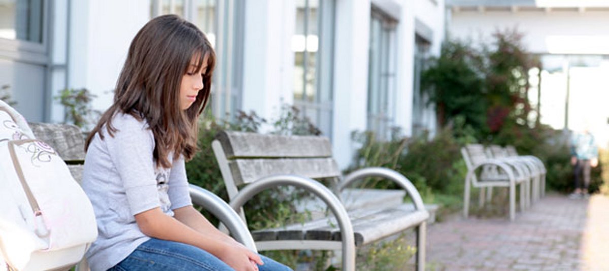 Ein Mädchen sitzt traurig auf einer Bank