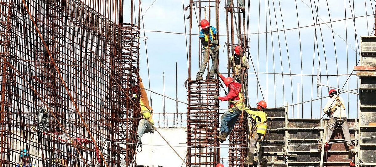 Auf dem Foto sind Bauarbeiter zu sehen, die kletternd an einer Baukonstruktion arbeiten.