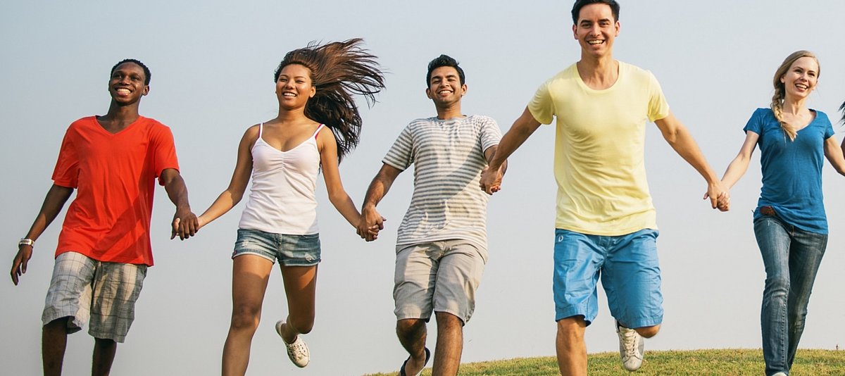 Eine Gruppe junger Menschen rennt über eine Wiese, sich an den Händen haltend und lächelnd