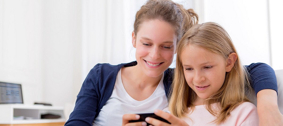 Mutter und Tochter sitzen auf dem Sofa und schauen gemeinsam auf ein Smartphone