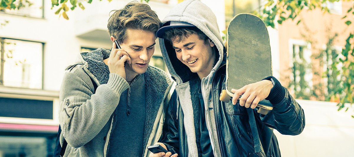 Zwei junge Männer in Lederjacke, mit Smartphones und Skateboard