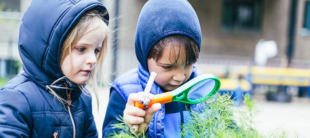 Zwei Kinder betrachten draußen Pflanzen mit einer Lupe