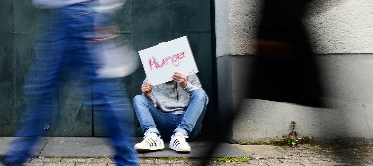 Junger Mann sitzt auf der Straße und hält ein Schild hoch, auf dem Hunger steht