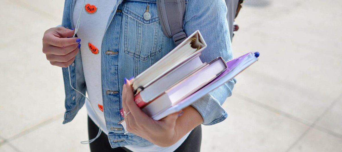 Auf dem Foto ist eine Schülerin zu sehen, die Bücher im Arm hält.