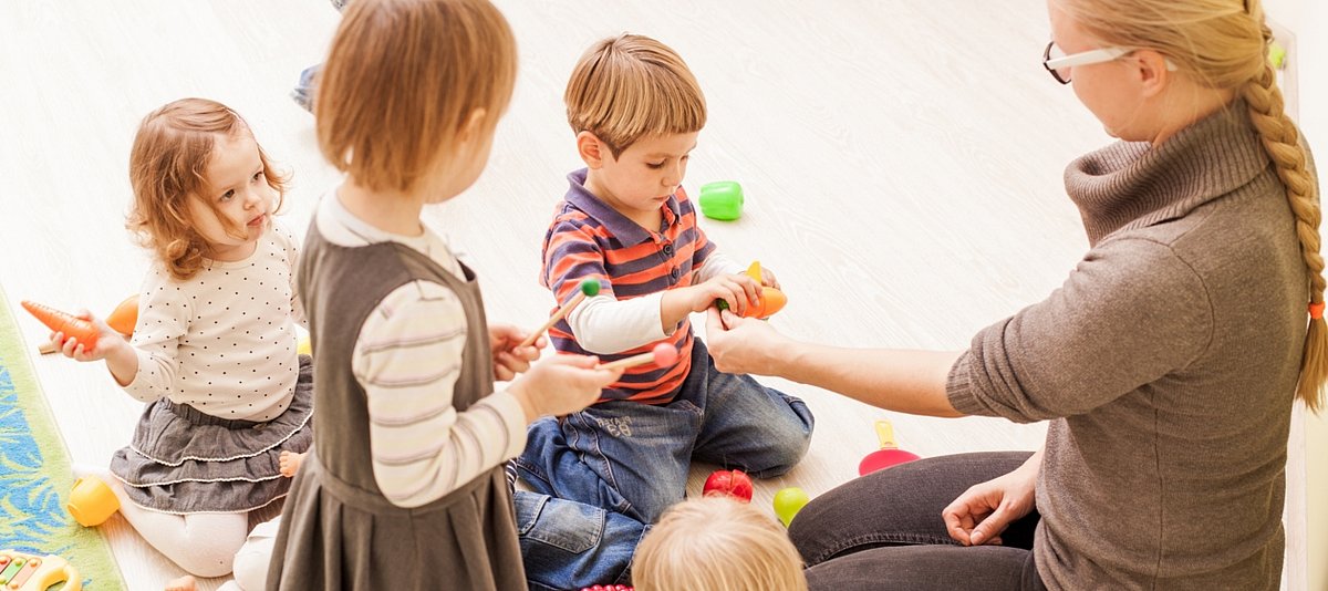 Eine Erzieherin sitzt mit drei spielenden Kindern auf dem Boden