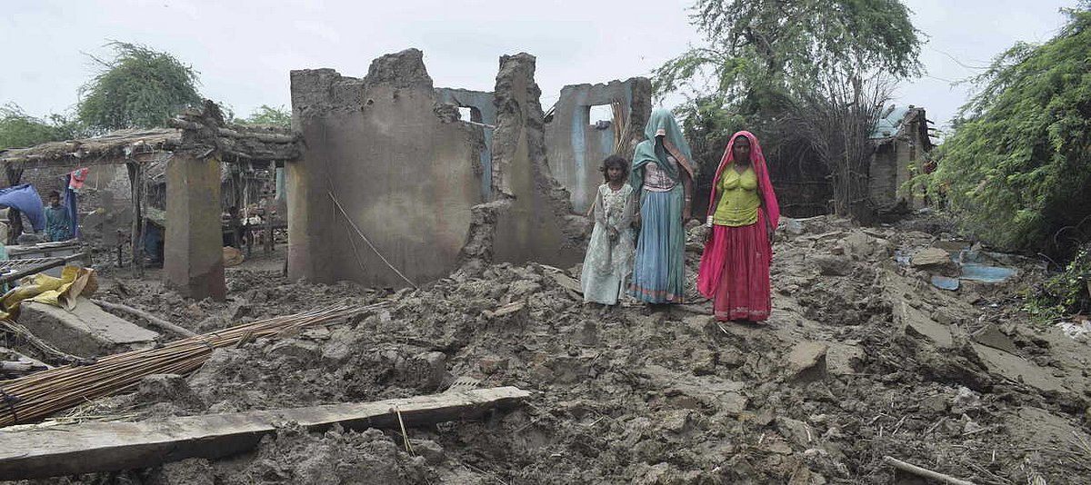 Auf dem Bild sind Trümmer von Gebäuden zu sehen, auf welchen drei Frauen stehen.