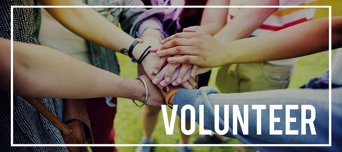 Hinter dem eingerahmten Wort 'Volunteer' legen Jugendliche die Hände aufeinander