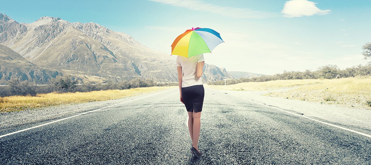 Frau geht mit regenbogenfarbenem Regenschirm eine Straße entlang