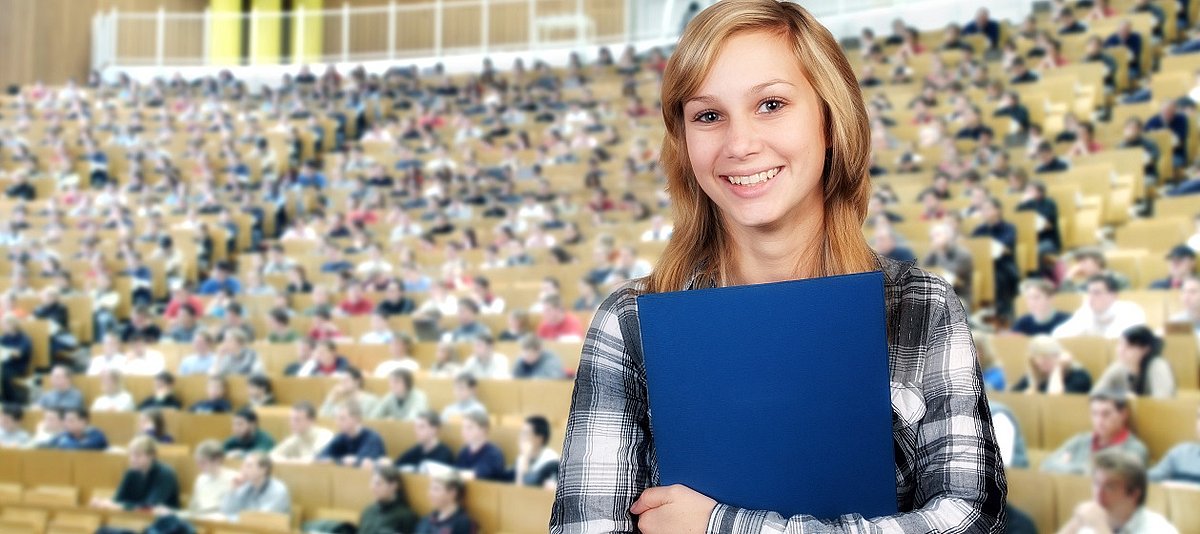 Eine junge Studentin steht im gut gefüllten Hörsaal.