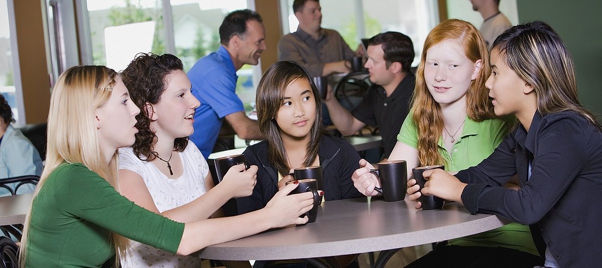 Eine Gruppe Mädchen sitzt um den Tisch und unterhält sich.