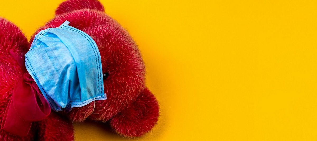 Ein roter Teddybär trägt eine Atem-Schutzmaske