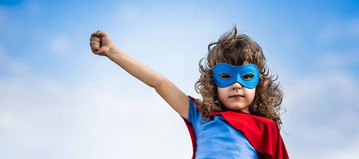 Ein Kind in Superheld-Verkleidung streckt einen Arm in die Luft