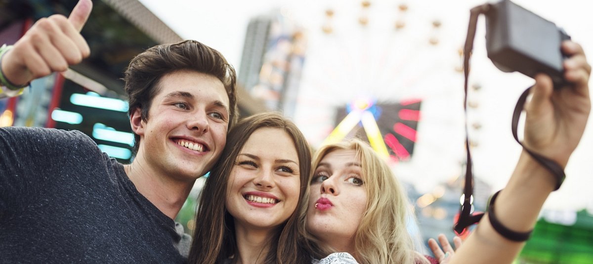 Drei Jugendliche nehmen mit einer Kamera ein Selfie auf und posieren lächelnd dafür