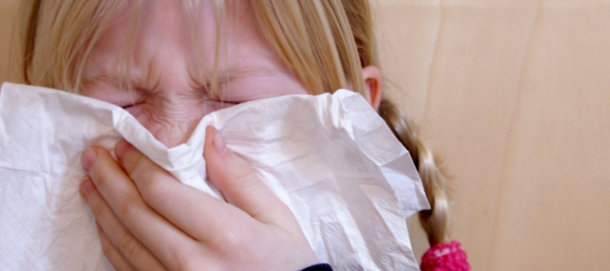 Ein Mädchen putzt sich die Nase mit der Hilfe eines Taschentuchs.