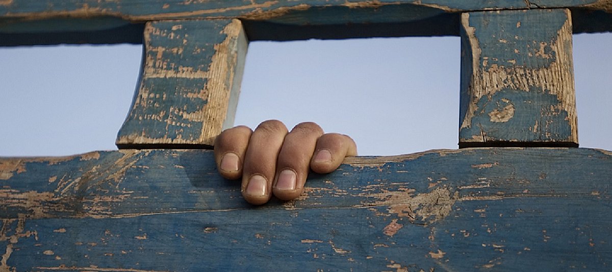 Eine Hand greift durch ein Loch in der Holzwand