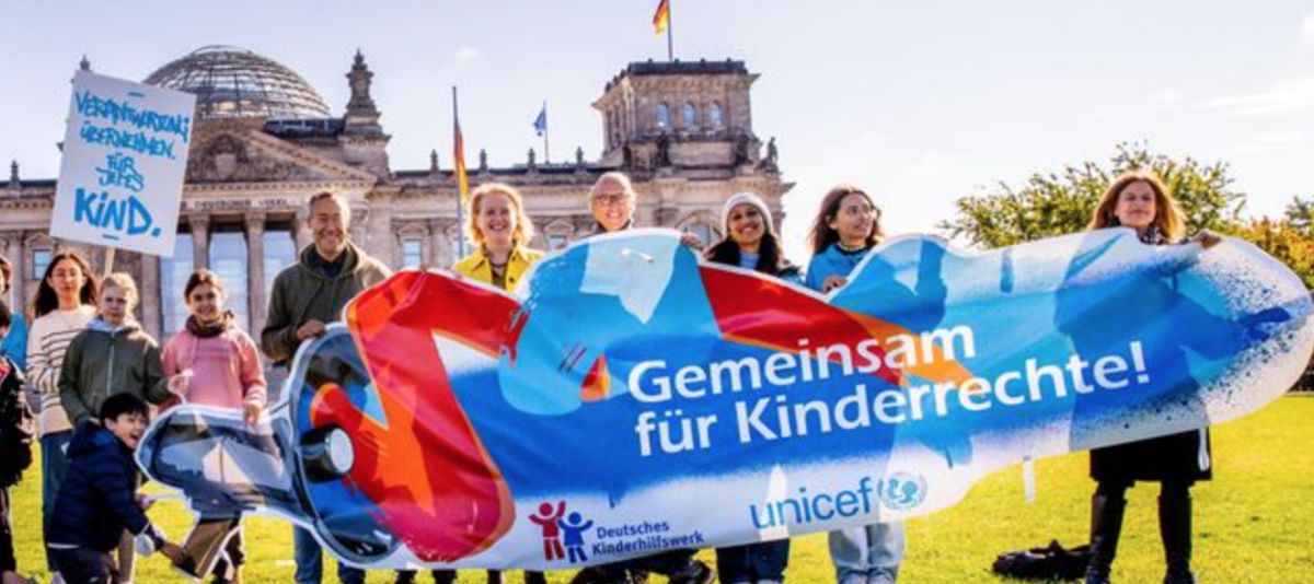 Menschen vor dem Deutschen Bundestag halten ein Banner für Kinderrechte hoch