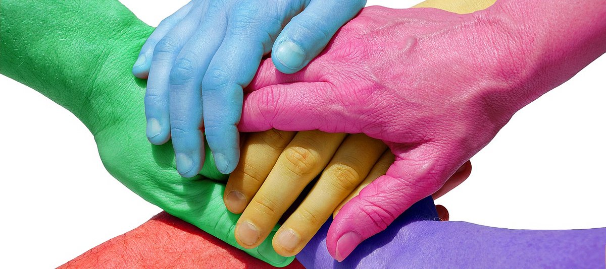 Sechs farbig angemalte Hände liegen aufeinander und zeigen damit Teamgeist.
