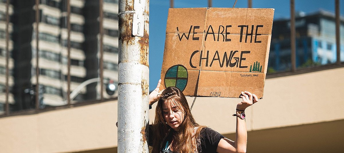 Eine Jugendliche hält ein Schild in die Höhe auf dem steht 'We are the Change. Solutions Now!'