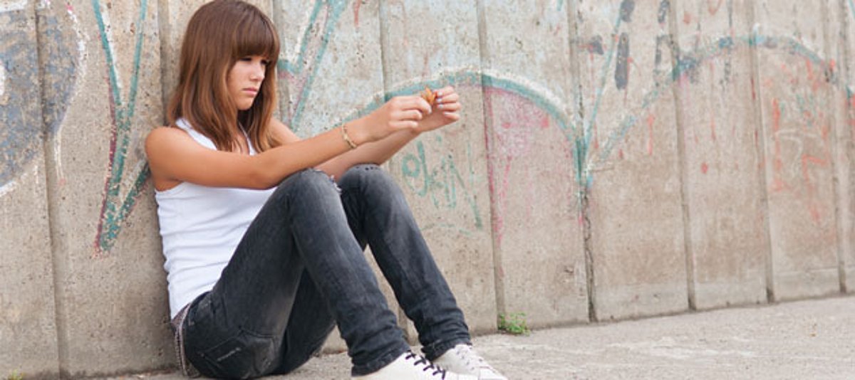 Ein junges Mädchen sitzt abgenervt vor einer Betonwand