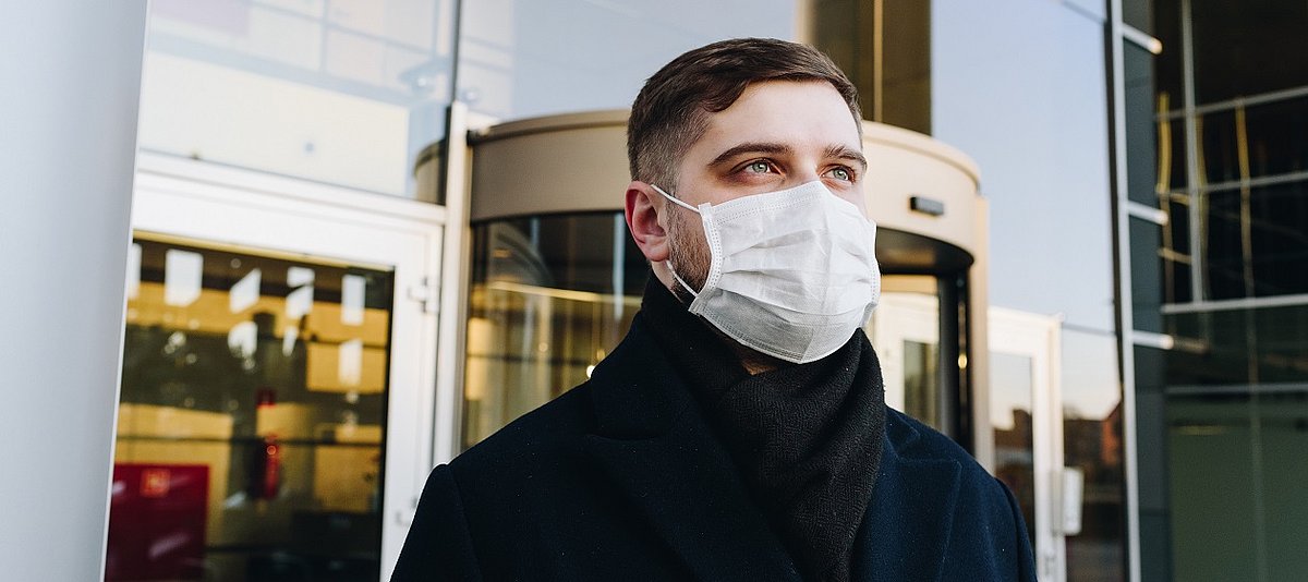 Mann mit einer Atemschutzmaske vor einem modernen Gebäude