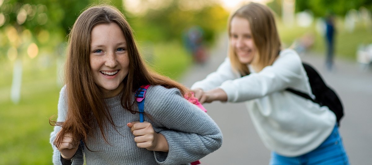 Zwei Schülerinnen mit Rucksäcken spielen draußen