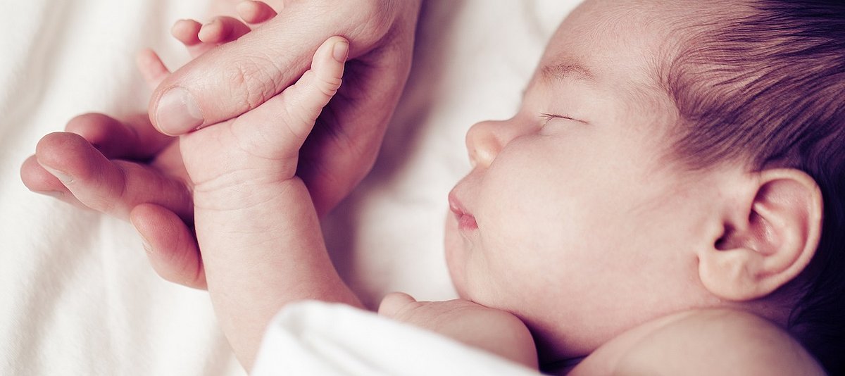 Die Hand eines schlafenden Neugeborenen liegt in einer Erwachsenenhand.