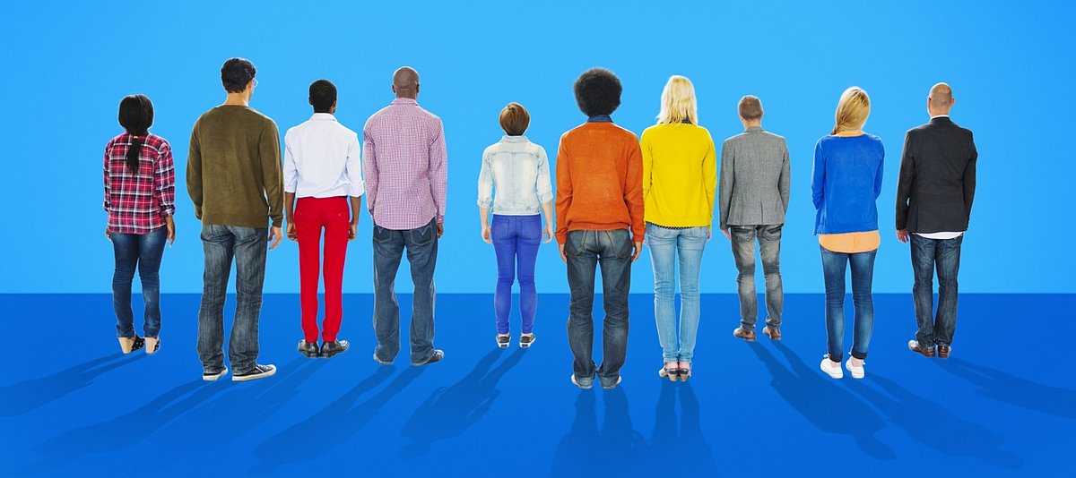 Zehn Menschen mit farbigen Kleidungsstücken stehen vor einem blauen Hiintergrund, mit dem Rücken zum Betrachter