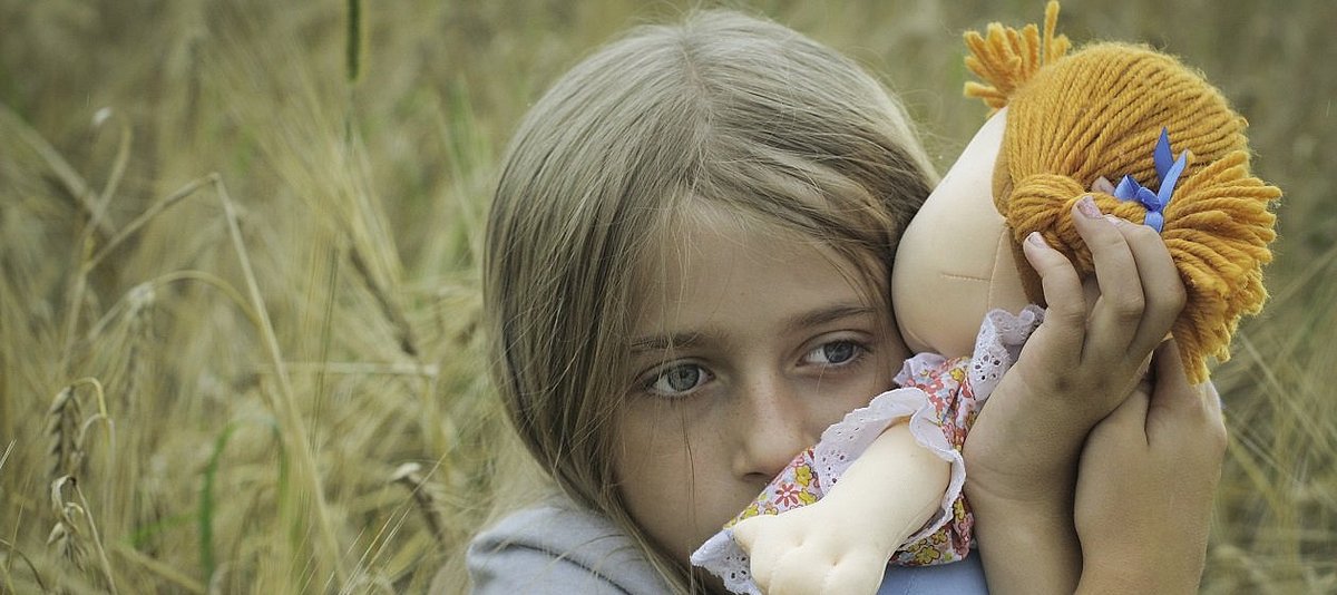ein kleines Mädchen schaut traurig und drückt eine Puppe an sich