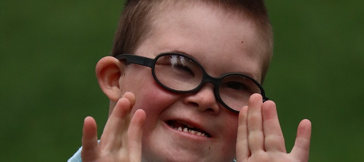 Ein Kind mit Down-Syndrom lacht in die Kamera