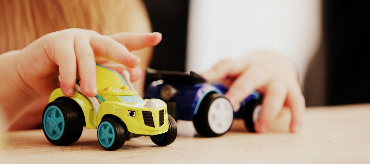 Nahaufnahme eines kleinen Kindes, das mit zwei Spielzeugautos spielt