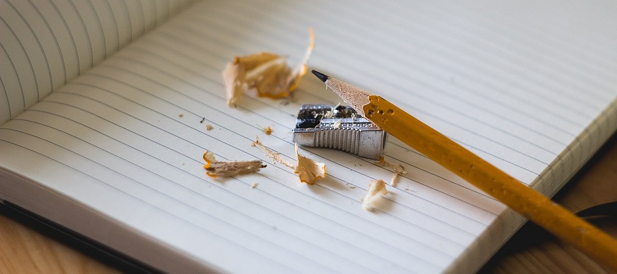 Auf einem Schreibheft liegen ein frisch angespitzter Bleistift und ein Spitzer