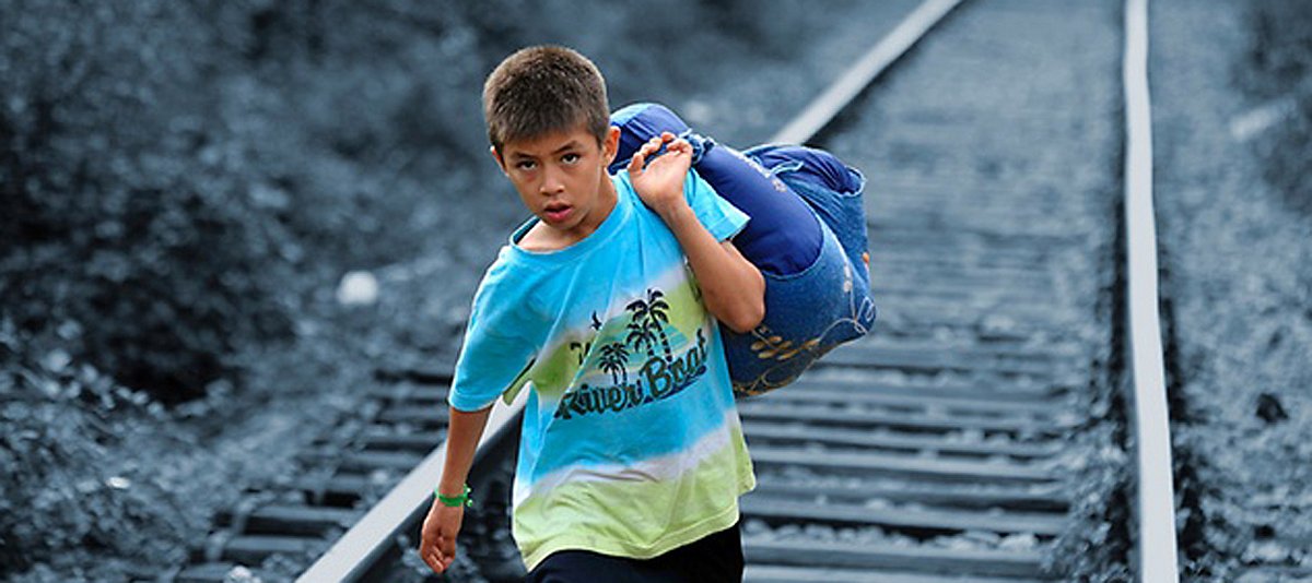 Ein Kind trägt seine verbliebene Kleidung huckepack über Schienen
