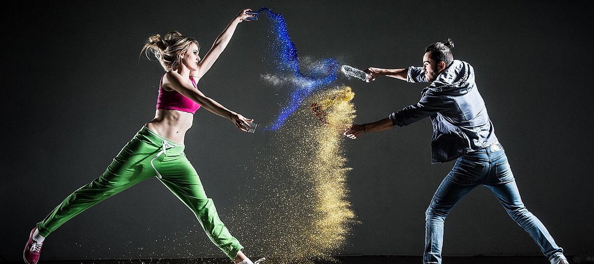 Zwei junge Menschen tanzen miteinander, zwischen ihnen sind bunte Farben in der Luft