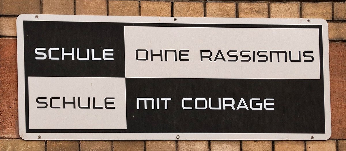 Auf einem schwarz-weißen Metallschild steht: "Schule ohne Rassismus. Schule mit Courage"