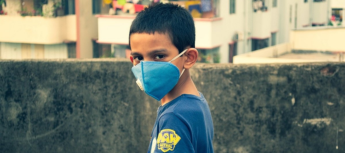 Junge mit Atemschutzmaske steht auf Balkon und dreht sich zur Kamera um