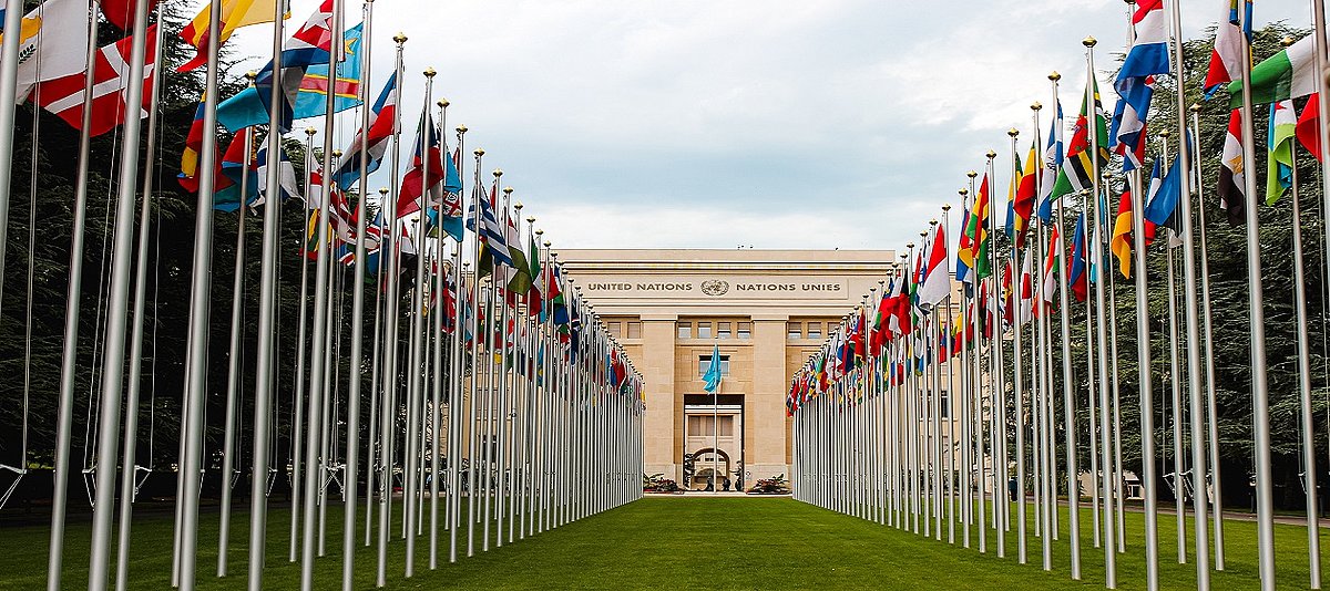 Vorderansicht des Palais des Nations in Genf. Links und rechts zulaufende Flaggend er Mitgliedsstaaten