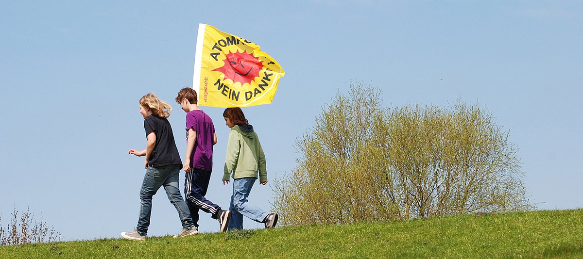 Drei Jugendliche mit einer Anti-Atomkraft-Fahne spazieren zusammen auf einer Wiese.