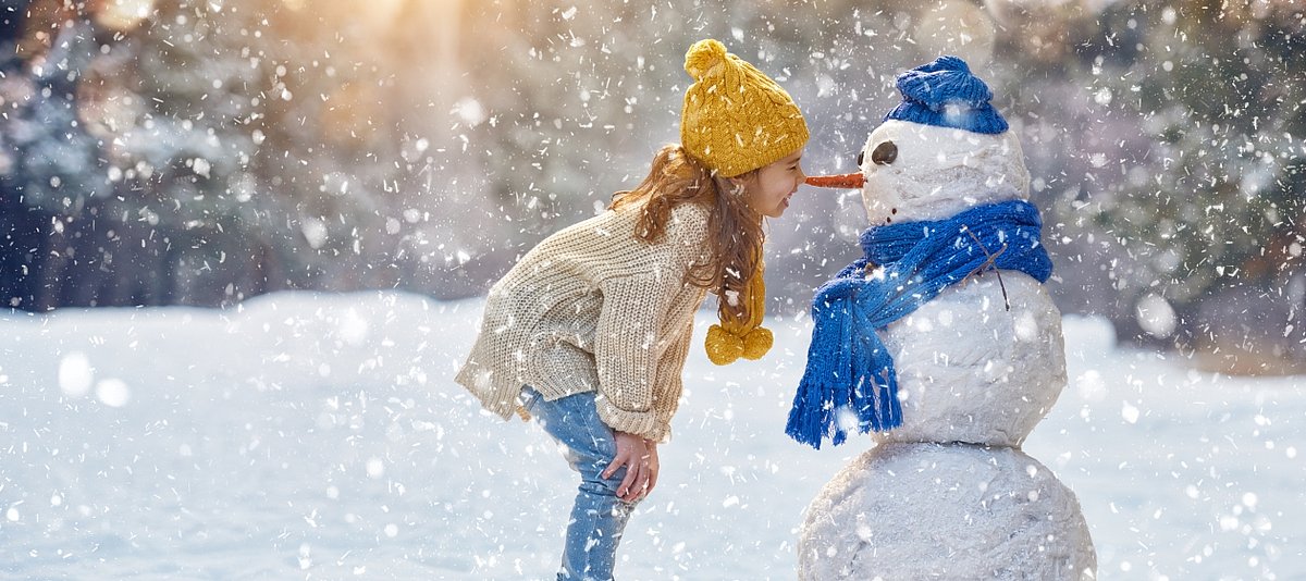 Ein Mädchen in Winterlandschaft spielt mit einem Schneemann
