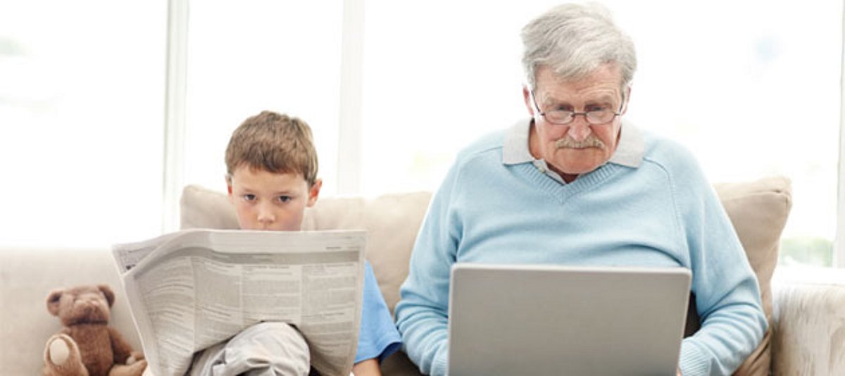 Großvater mit dem Laptop und Enkel mit der Zeitung