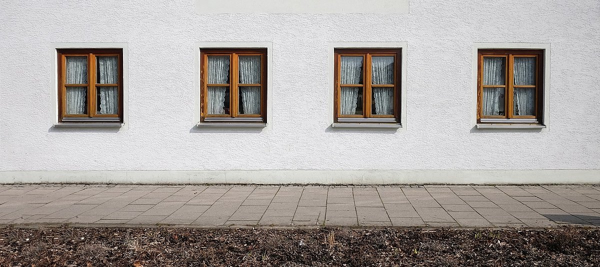 Eine Häuserfront mit vier gleichen Fenstern mit zugezogenen Vorhängen