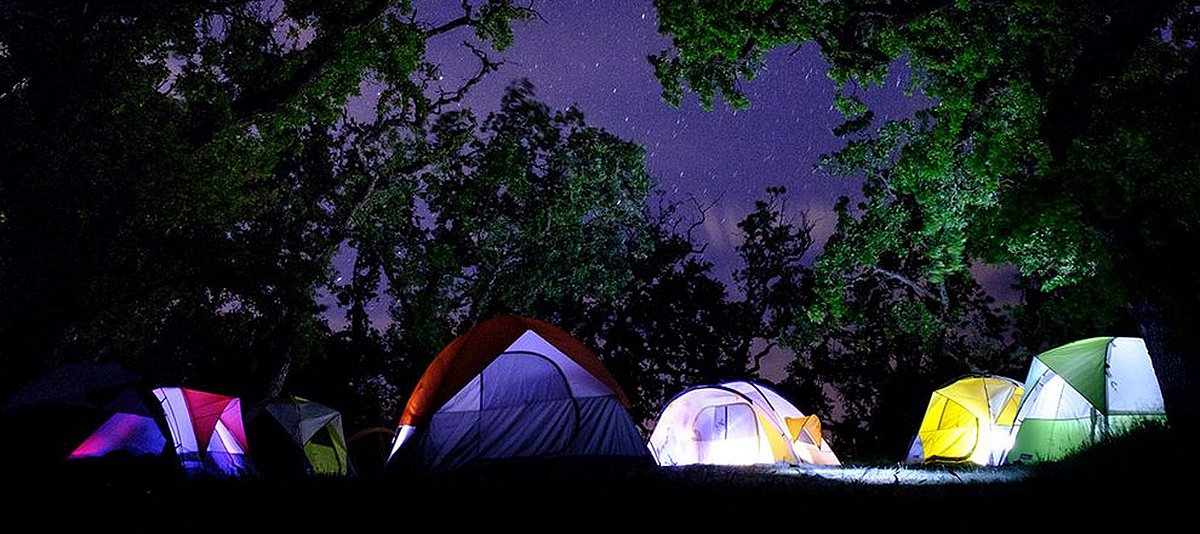 Beleuchtete Zelte unter einem Nachthimmel mit Bäumen 