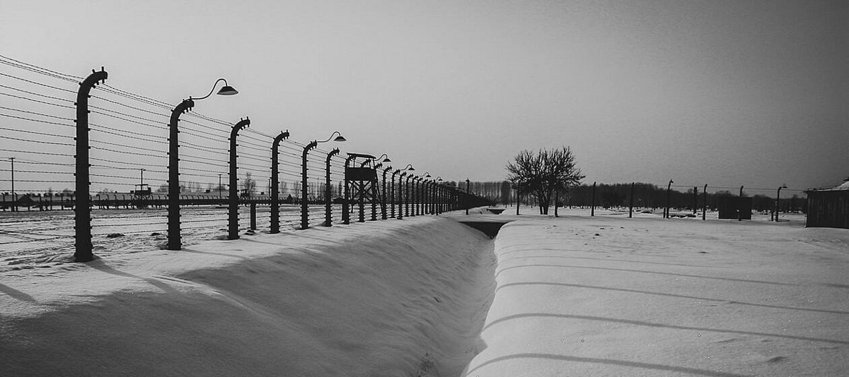 Stacheldrahtzaun und Graben im verschneiten KZ Auschwitz II - Birkenau