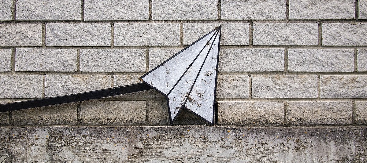 Papierflieger aus Metall vor einer Backsteinwand