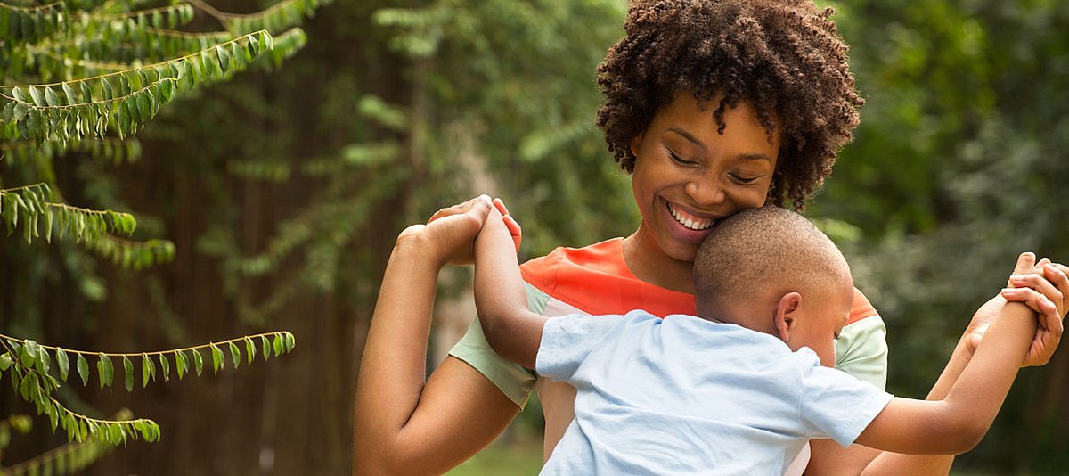 Eine Mutter afroamerikanischer Herkunft hält im Park ihren Sohn auf dem Schoss und lächelt.