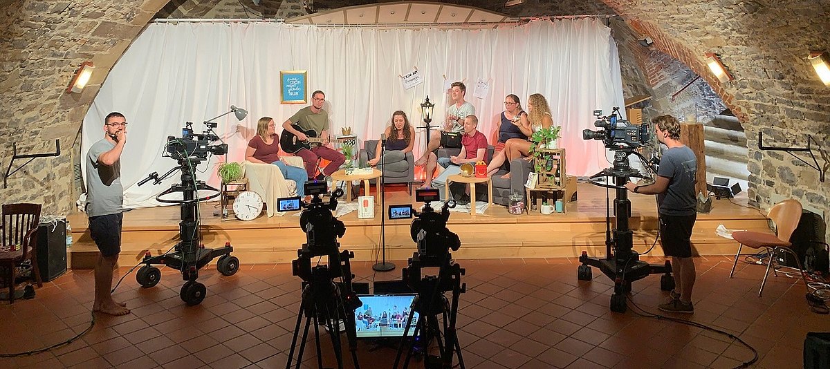 Eine Gruppe von Jugendlichen sitzen in einer Gesprächssituation auf einer Bühne und werden von einem Kamerateam gefilmt