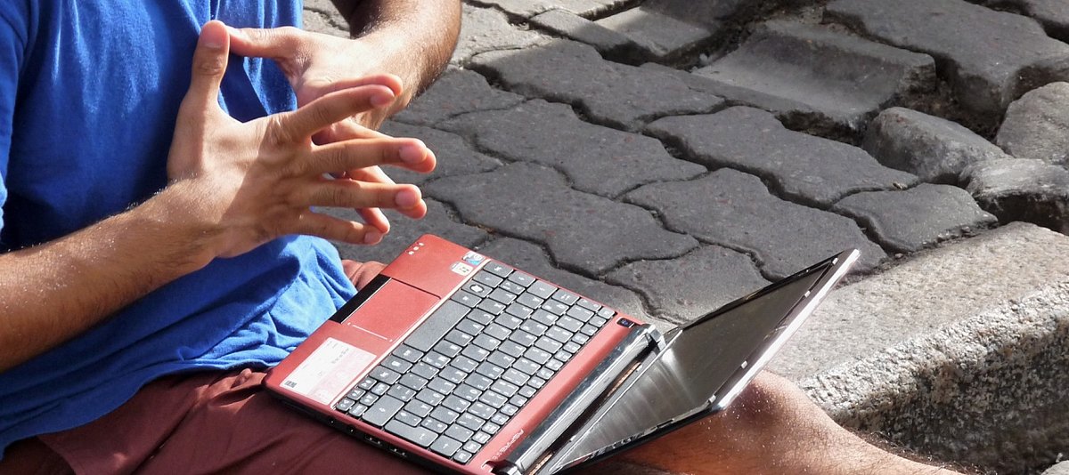 Ein Mann sitzt draußen auf Asphalt und hat einen Laptop auf den Beinen