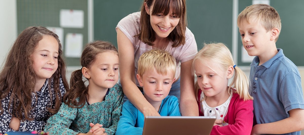 Eine Lehrerin zeigt einer Gruppe von Schülerinnen und Schülern etwas auf einem Laptop