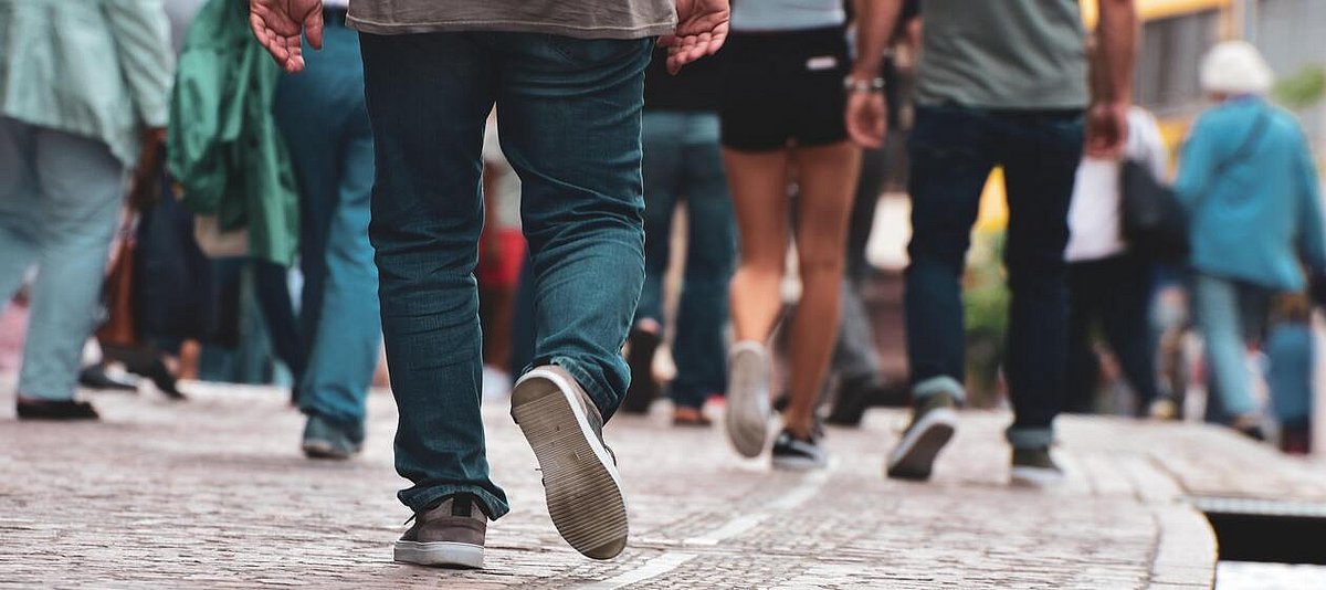 Auf dem Foto sind die Beine verschiedener Menschen zu sehen, die auf einer Straße laufen.